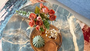 A round marble coffee table with a vase of roses and decorative items. - Skyline Haven 2BHK 28th Floor + Pool (Gandhinagar)