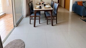 A dining area with a table set for four, a ceiling fan, and a sliding glass door leading to an outdoor area. - Skyline Haven 2BHK 28th Floor + Pool (Gandhinagar)
