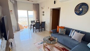 A modern living room with a sofa, coffee table, and ceiling fan. - Skyline Haven 2BHK 28th Floor + Pool (Gandhinagar)