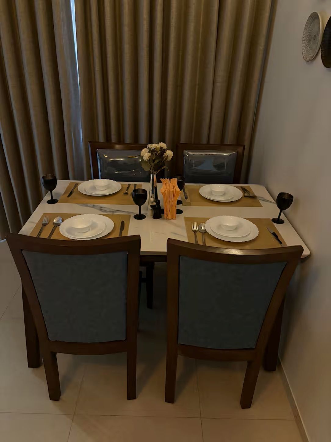 A dining table set for four with chairs, a vase with flowers, and a glass of wine.