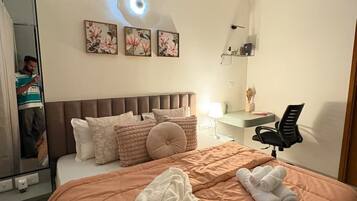 Une chambre à coucher comprenant un lit, un bureau, une chaise, un ventilateur de plafond et des œuvres d’art accrochées au mur.