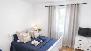 Een slaapkamer met twee bedden, een kroonluchter, een televisie en een raam met gordijnen.