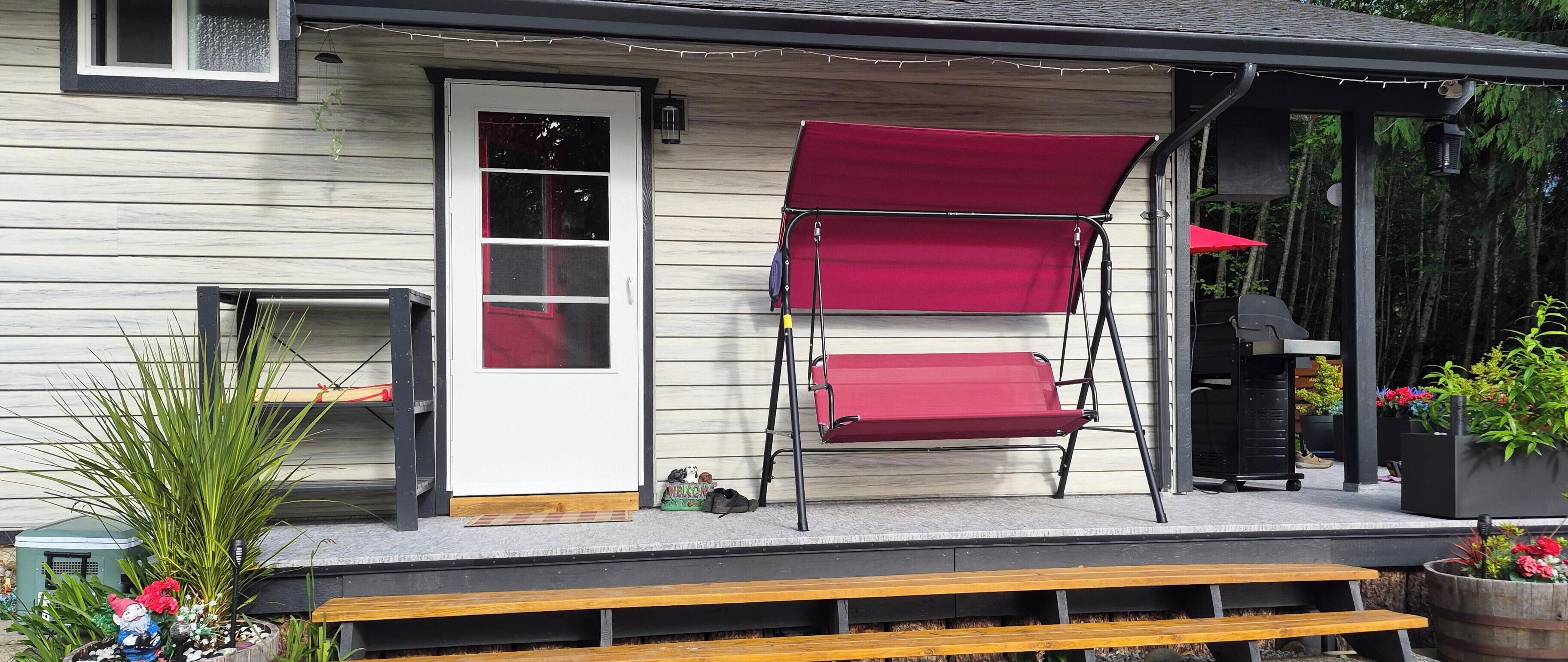 Une véranda avec une balançoire rouge, un banc et une porte dotée d’une fenêtre.