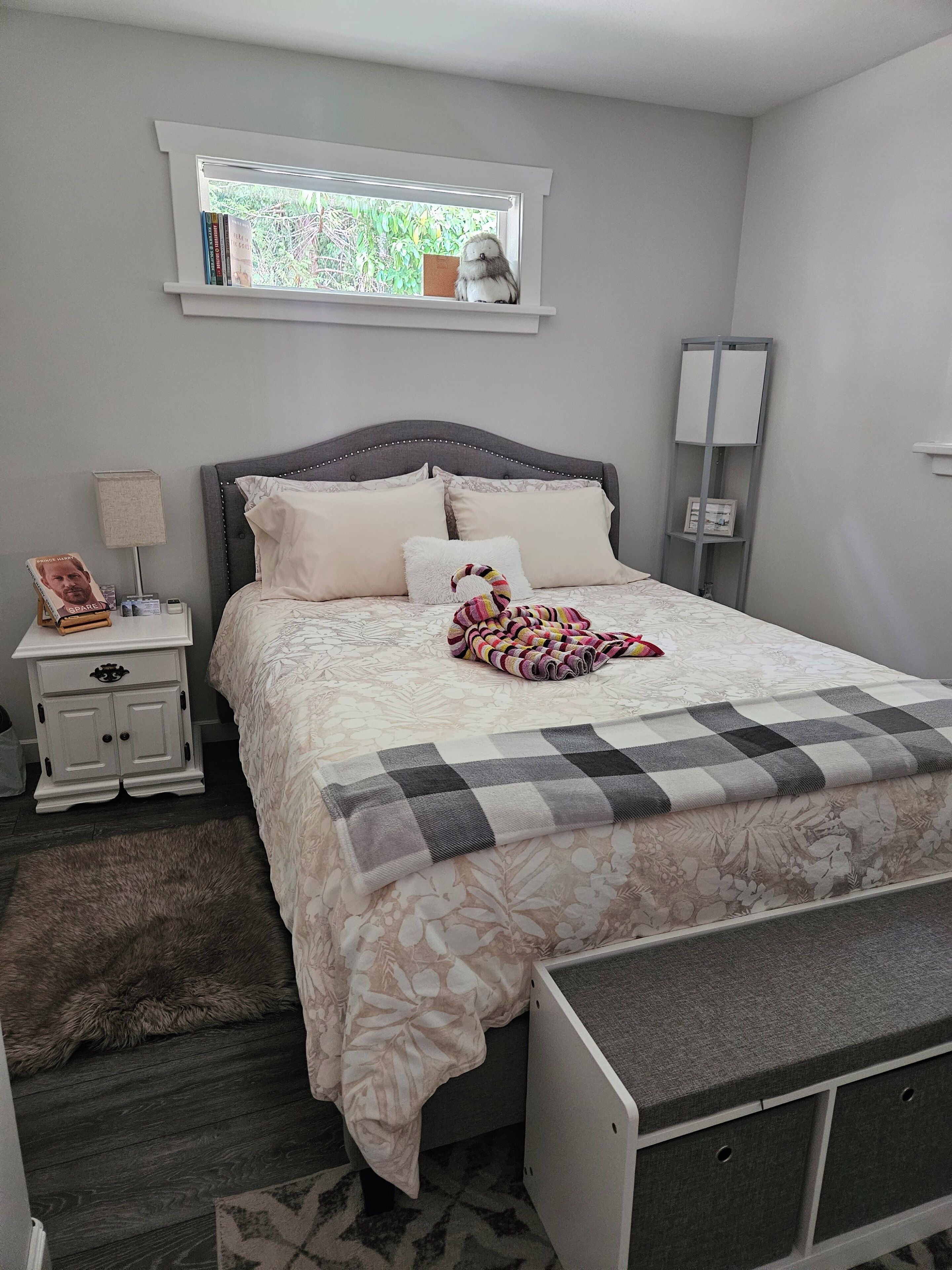 A bedroom with a bed, a nightstand, a lamp, a window, a bookshelf, and a dresser.