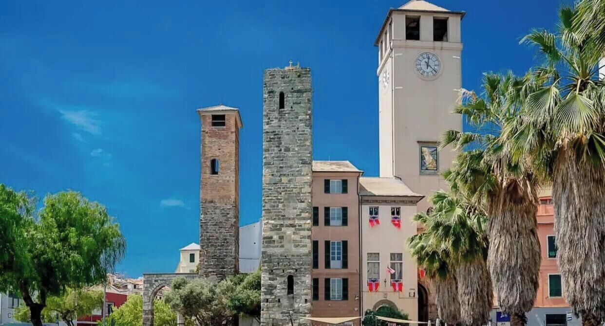 Eine historische Stadt mit einem markanten Glockenturm, einem Steinhaus und Palmen.