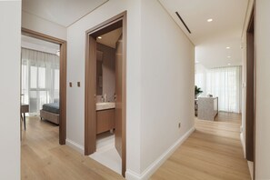 A modern hotel room with a wooden floor, a large bed, a bathroom with a vanity, and a view of the hallway. - Elegant 2BR Apartment with Sea View (Dubai)