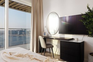 A bedroom with a bed, a desk, a chair, a television, and a view of the city. - Elegant 2BR Apartment with Sea View (Dubai)