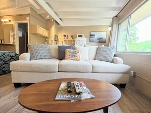 Een woonkamer met een bank, een salontafel met tijdschriften, en een keuken op de achtergrond.