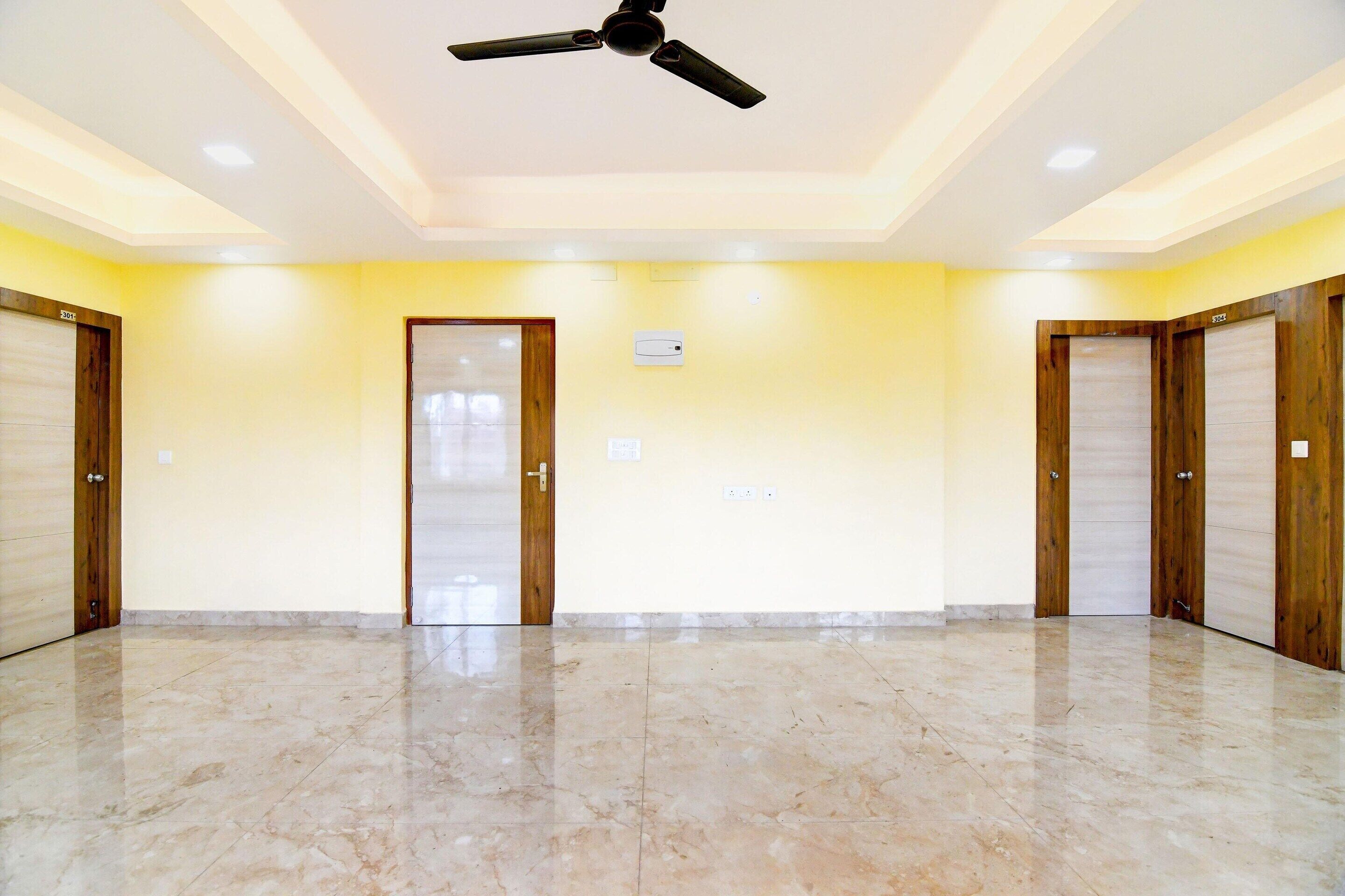 A spacious room with a ceiling fan, marble flooring, and wooden doors.