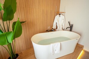 A modern bathroom with a freestanding bathtub, a towel, a wooden wall, and a plant. - Agorà Luxury Experience (Zafferana Etnea)