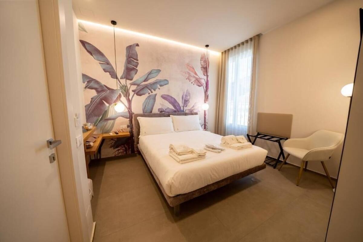 Quarto de hotel com cama, escrivaninha, cadeira e parede com um mural de folhagem tropical.