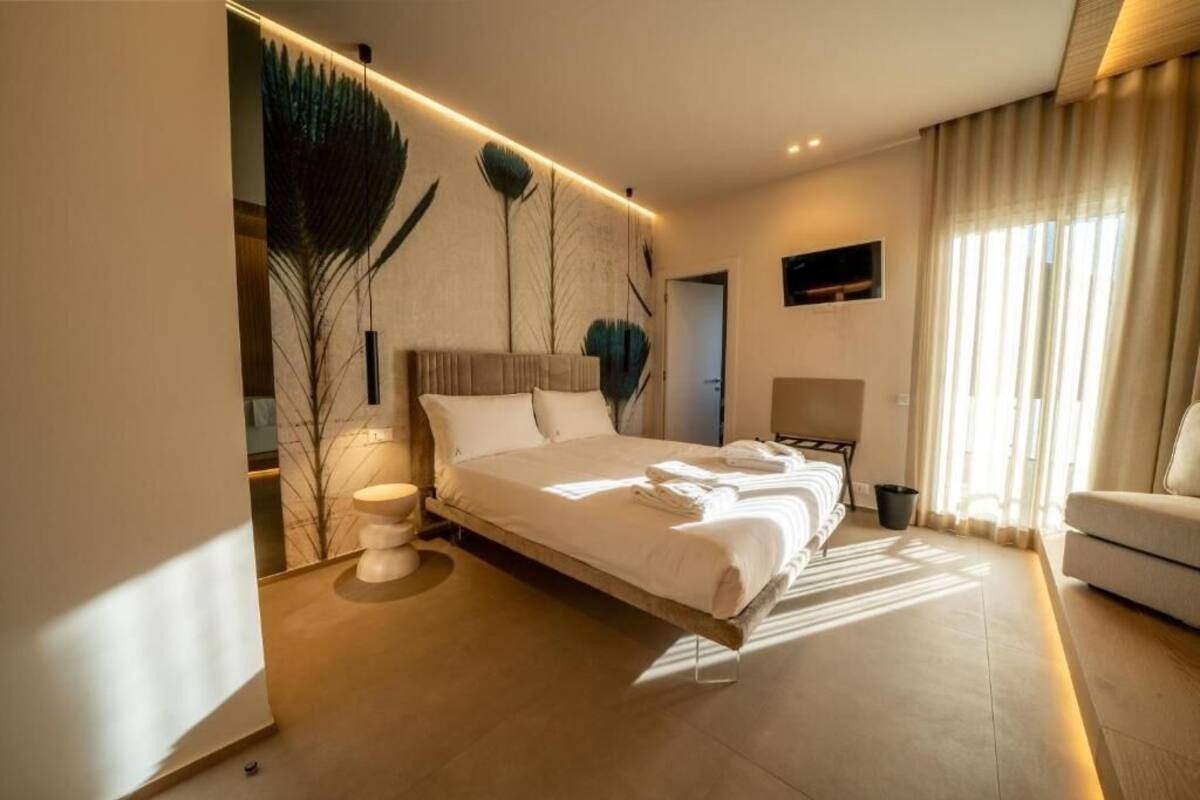Quarto de hotel moderno com uma cama grande, uma mesinha de cabeceira, uma televisão e vista para o exterior.