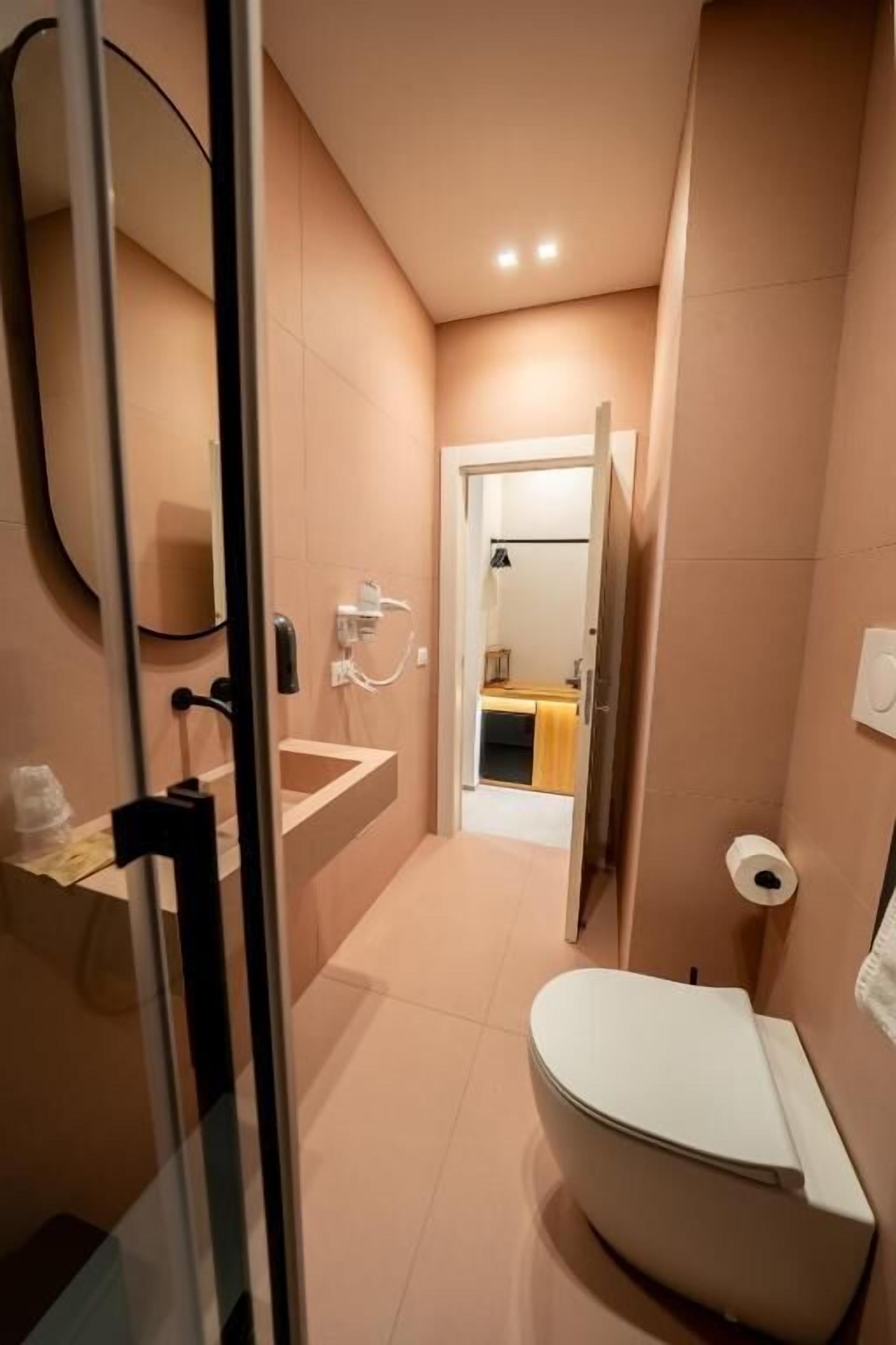 A compact bathroom with a toilet, sink, and shower area, featuring a glass partition and a visible door leading to another room.