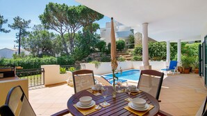 A patio with a round table set for dining, a pool, and a white building in the background. - Apartment 'Tulipa' with Private Pool, Wi-Fi, and Air Conditioning (Almancil)