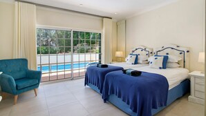 A hotel room with a large window, a pool view, a bed with blue bedding, a chair, and a nightstand. - Apartment 'Tulipa' with Private Pool, Wi-Fi, and Air Conditioning (Almancil)
