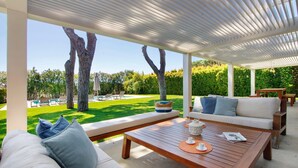 Zona relax esterna coperta con vista su piscina e vegetazione.
