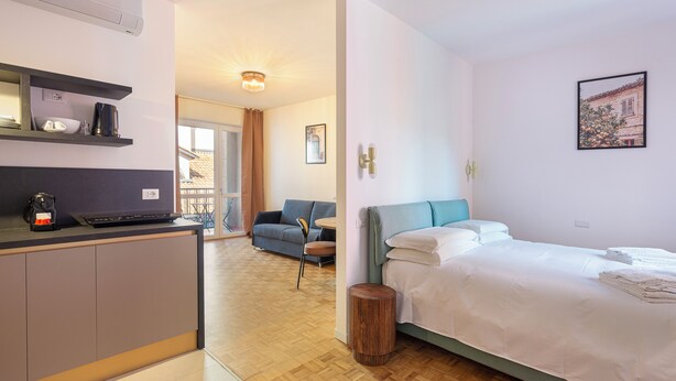 Ein modernes Hotelzimmer mit einer Küchenzeile, einem Bett, einer Couch und Blick ins Freie.