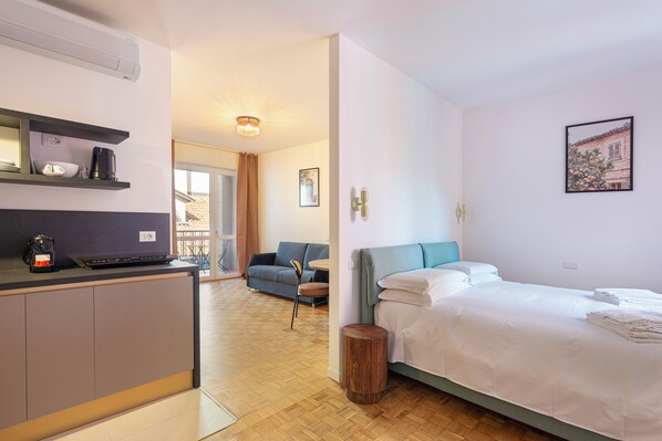 Ein modernes Hotelzimmer mit einer Küchenzeile, einem Bett, einer Couch und Blick ins Freie.