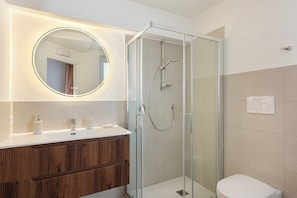 A modern bathroom with a glass-enclosed shower, a round mirror with built-in lighting, and a wooden vanity.