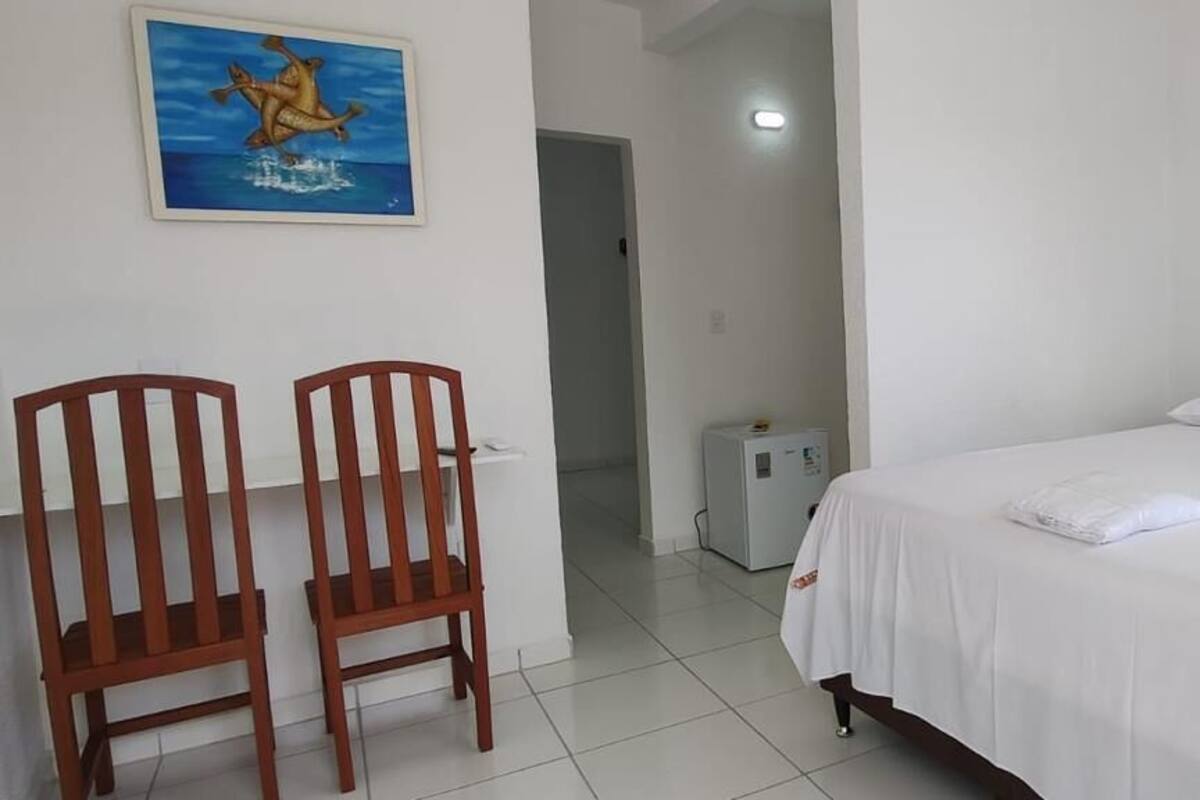 Une pièce comprenant un lit, deux chaises en bois, un petit radiateur blanc et un tableau accroché au mur.