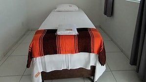 A single bed with a white mattress and a striped blanket, a pillow, and a small bedside table with a bottle. - Hotel Barra de São Miguel (Barra de São Miguel)