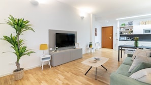 A modern living room with a flat-screen TV, a grey sofa, a coffee table, and a dining area with a kitchen in the background. - Narea 15 - [3 min from Arena & Piazza Bra] (Verona)