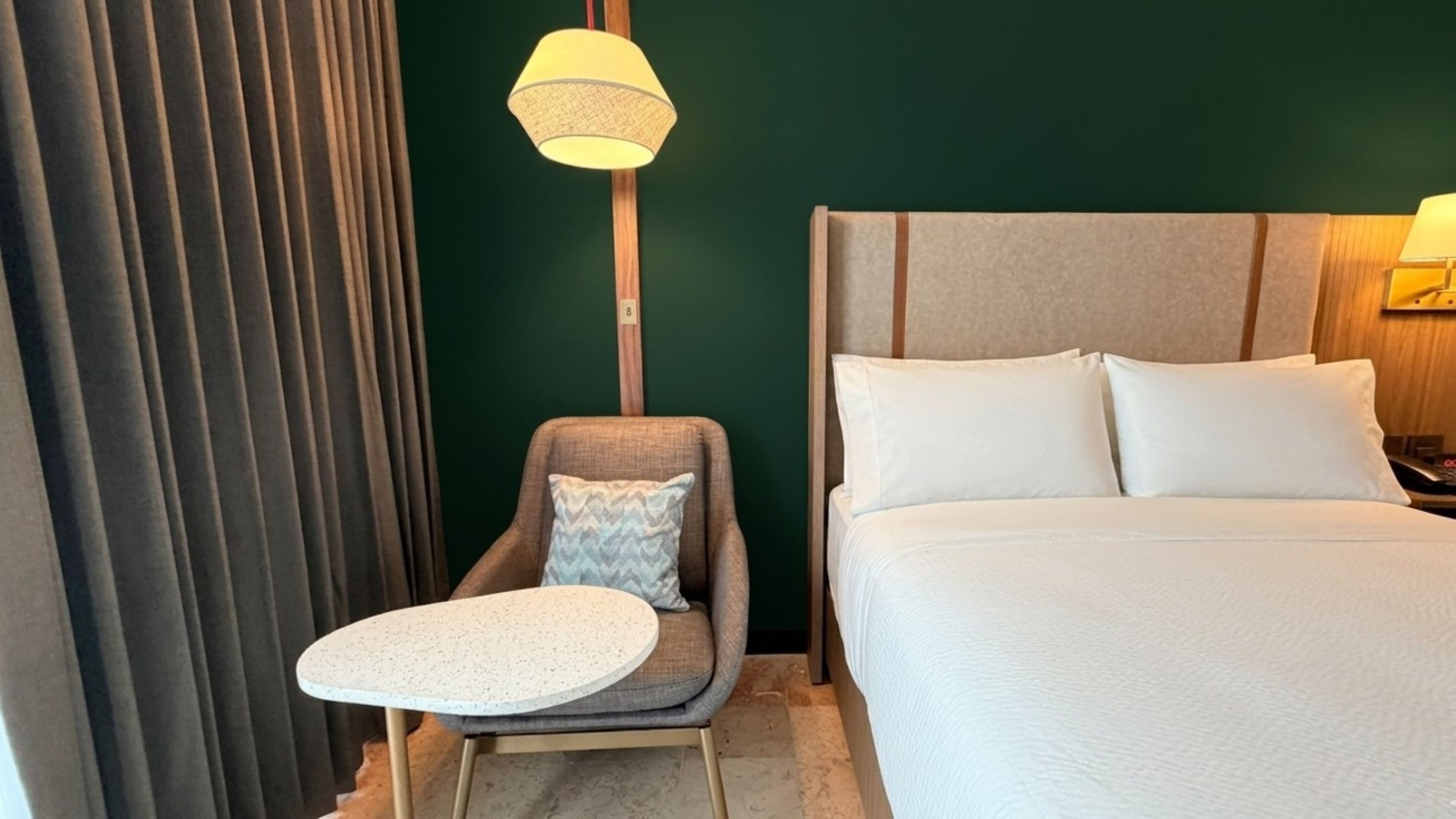 A hotel room with a bed, a small round table, a chair, a lamp, and a curtain.