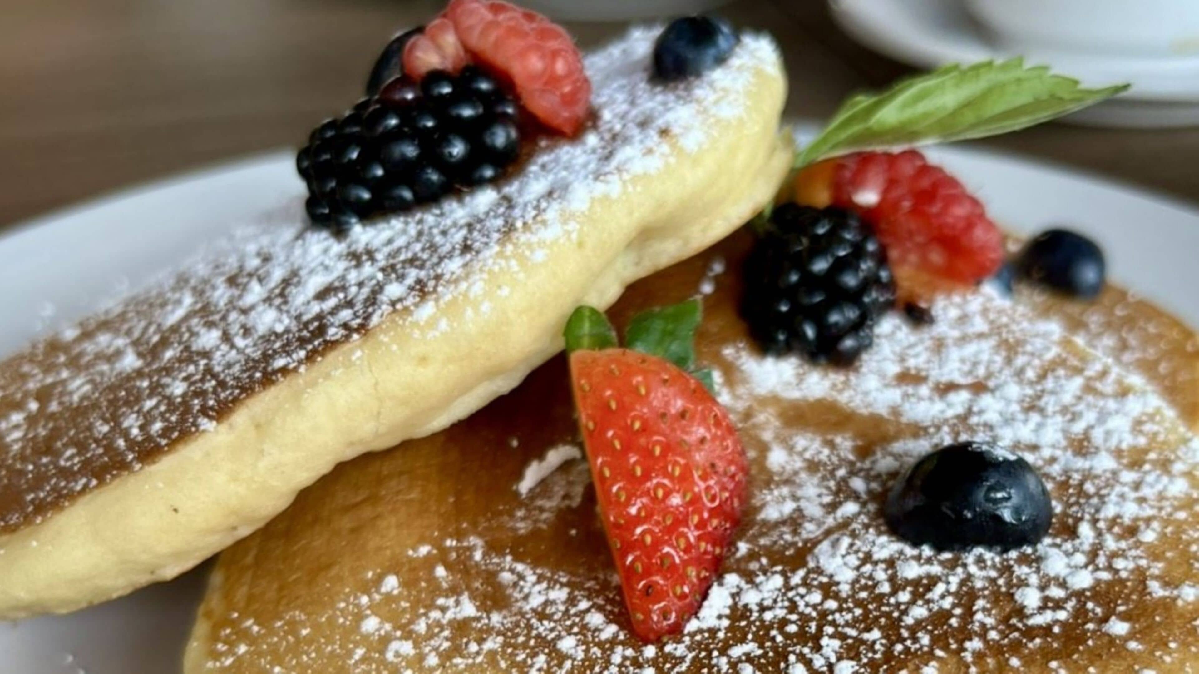 A plate of pancakes topped with blackberries, raspberries, blueberries, and strawberries, dusted with powdered sugar.
