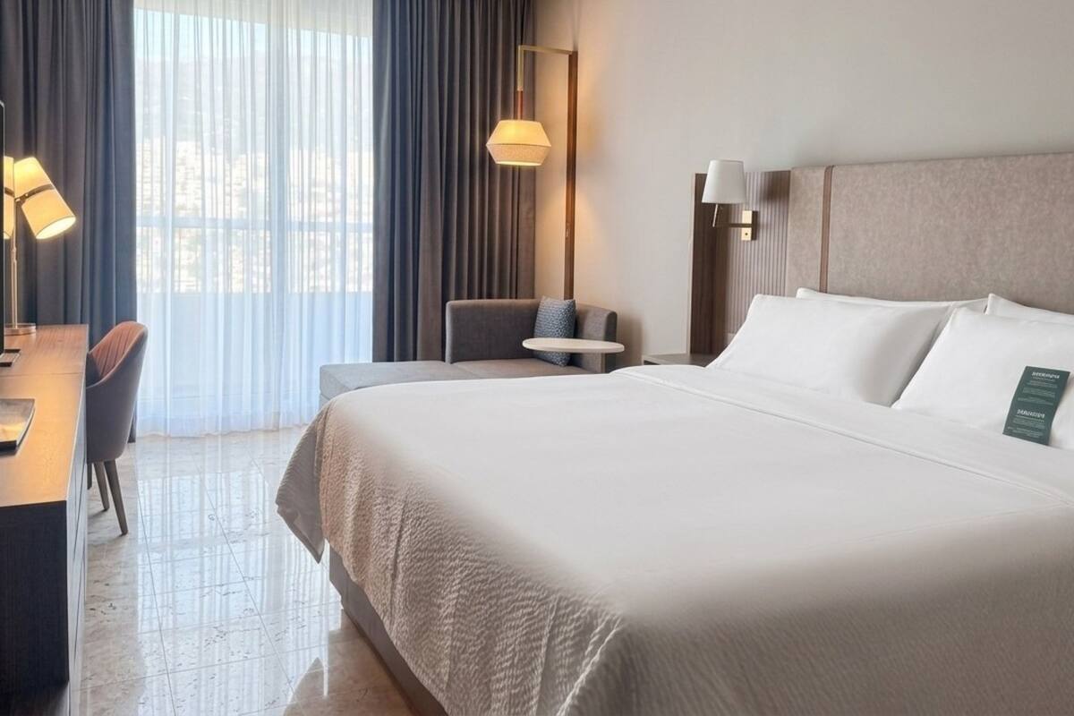 A hotel room with a large bed, a desk with a chair, a small table, and two lamps.