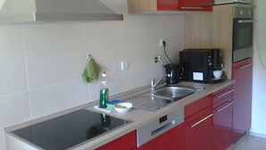 A modern kitchen with a stainless steel sink, a coffee maker, and red cabinets. - Apartment "For 4 Guests, 75 m²" with Shared Garden and Wi-Fi (Heeßen)