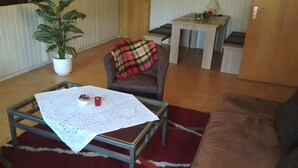 A living room with a glass-top coffee table, a brown leather sofa, a red and black plaid blanket on a brown leather chair, a potted plant, and a small table with a lamp and a laptop. - Apartment "For 4 Guests, 75 m²" with Shared Garden and Wi-Fi (Heeßen)