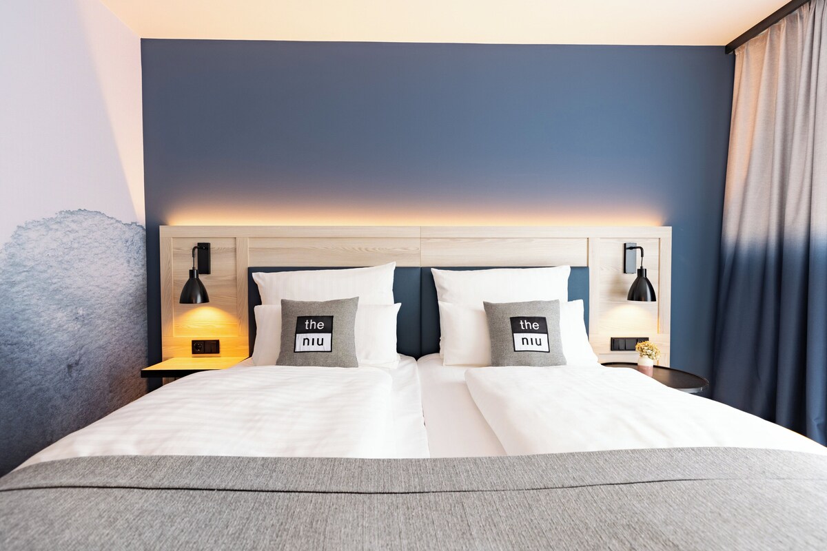 Quarto de hotel com uma cama grande, duas mesas de cabeceira com luminárias e uma cabeceira com design degradê.