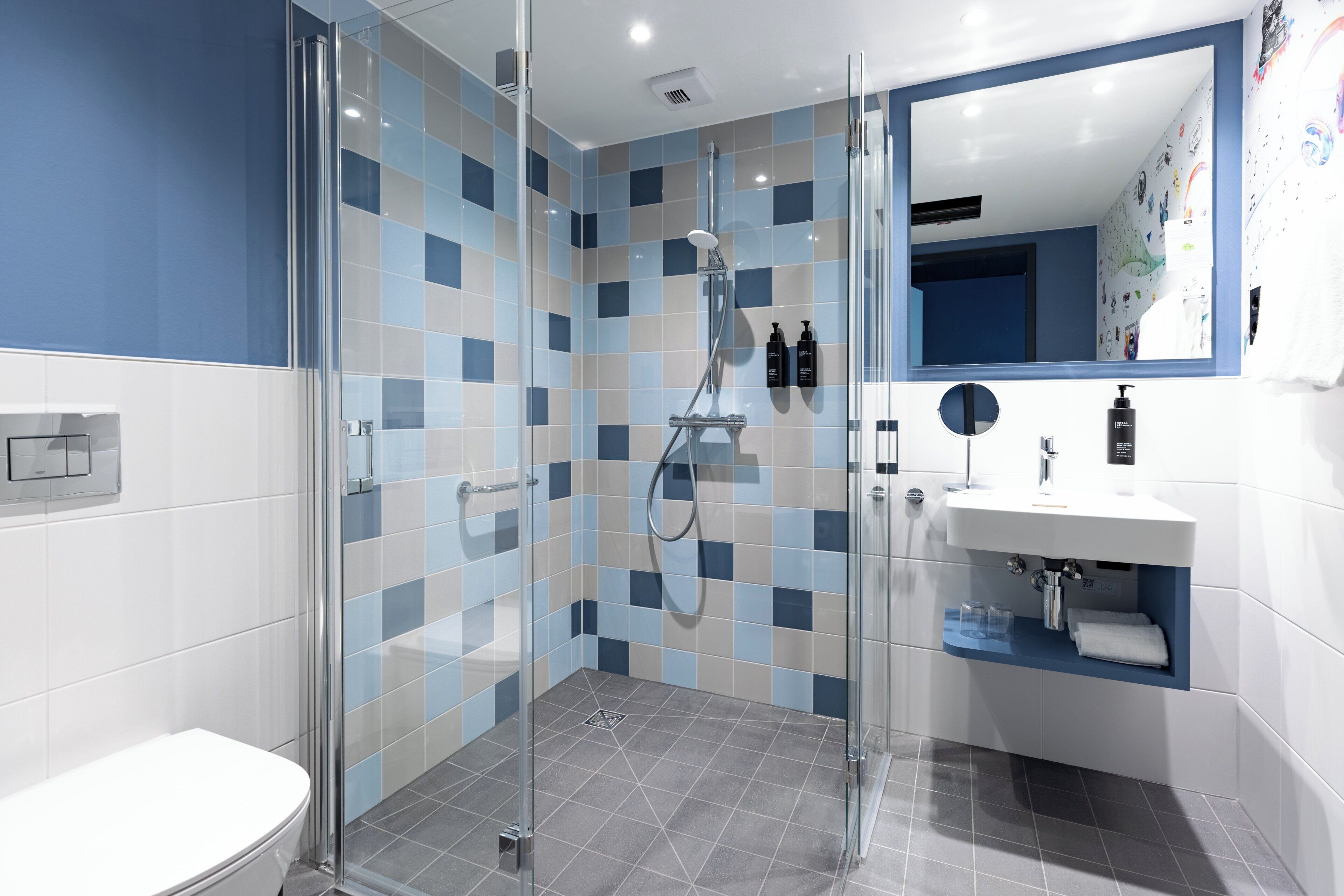 Ein modernes Badezimmer mit einer gläsernen Dusche, einem weißen Waschbecken mit Spiegel und einer blau-weißen Wand.
