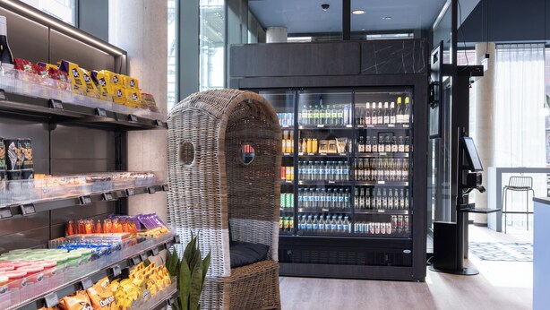 A modern retail space with shelves stocked with snacks, a refrigerated display case, and a wicker chair.