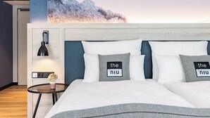 A hotel room with a bed, two pillows with text, a nightstand, a lamp, and a wall-mounted control panel.