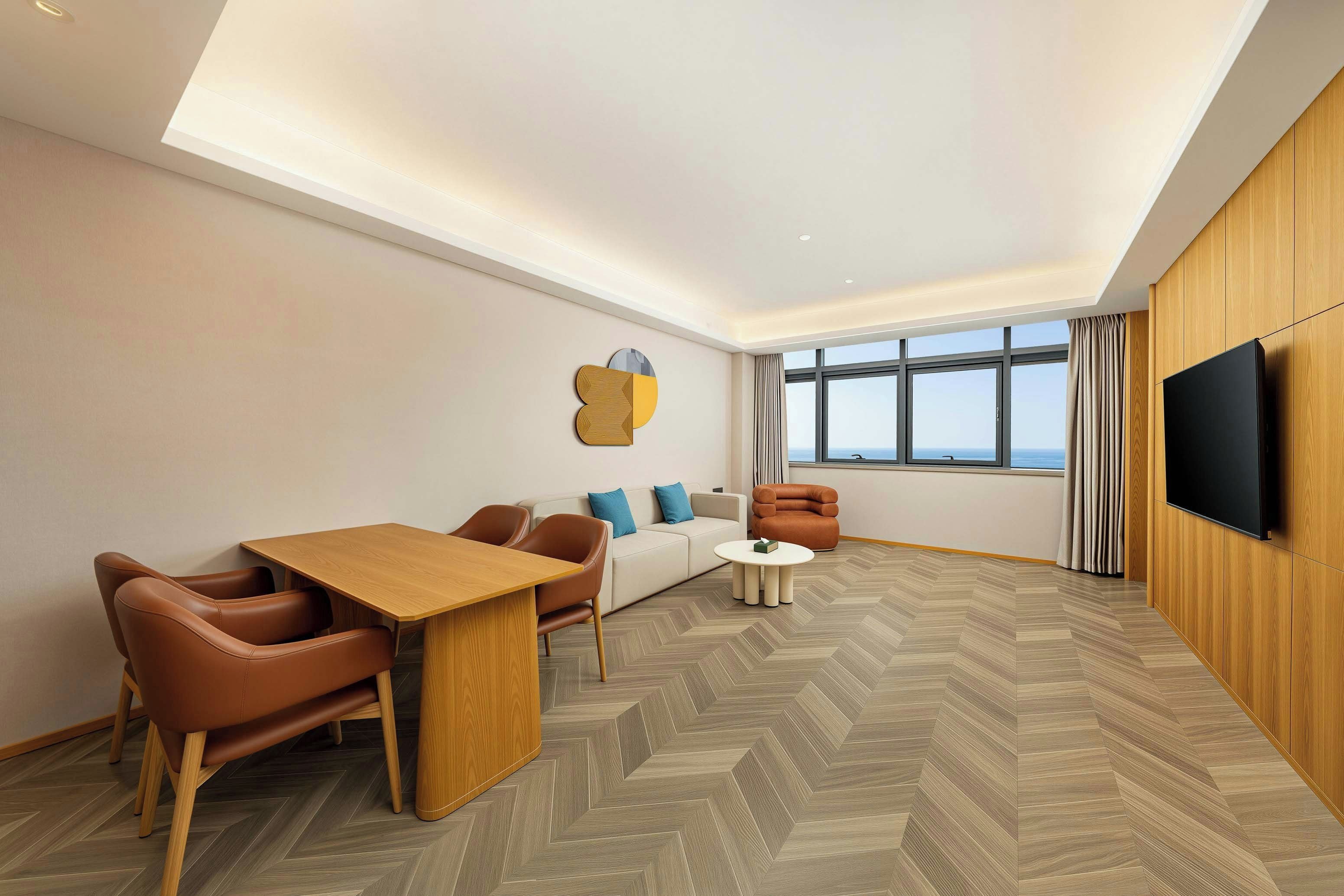 Habitación de hotel moderna con zona de comedor, sofá, sillón y un amplio ventanal con vistas.