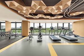 A modern gym with treadmills, elliptical machines, and dumbbells, large windows, and a geometric ceiling design. - EVEN Hotel Yantai Golden Coast By IHG (Yantai)