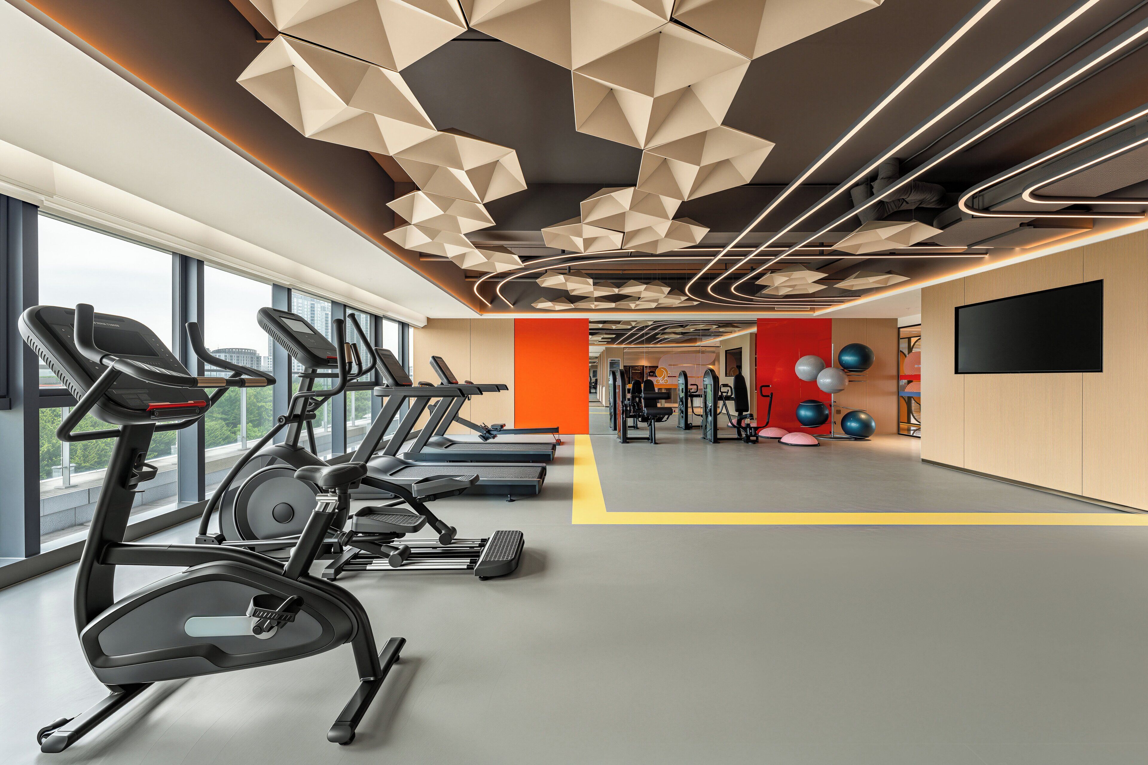 A gym with treadmills, exercise balls, and a TV screen.