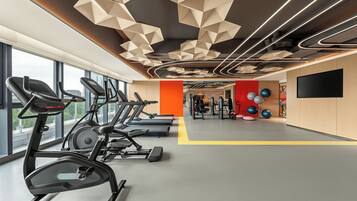 A gym with treadmills, exercise balls, and a TV screen.