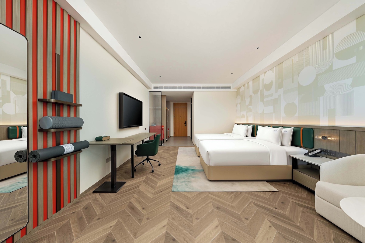 Quarto de hotel com cama, escrivaninha, cadeira e televisão.