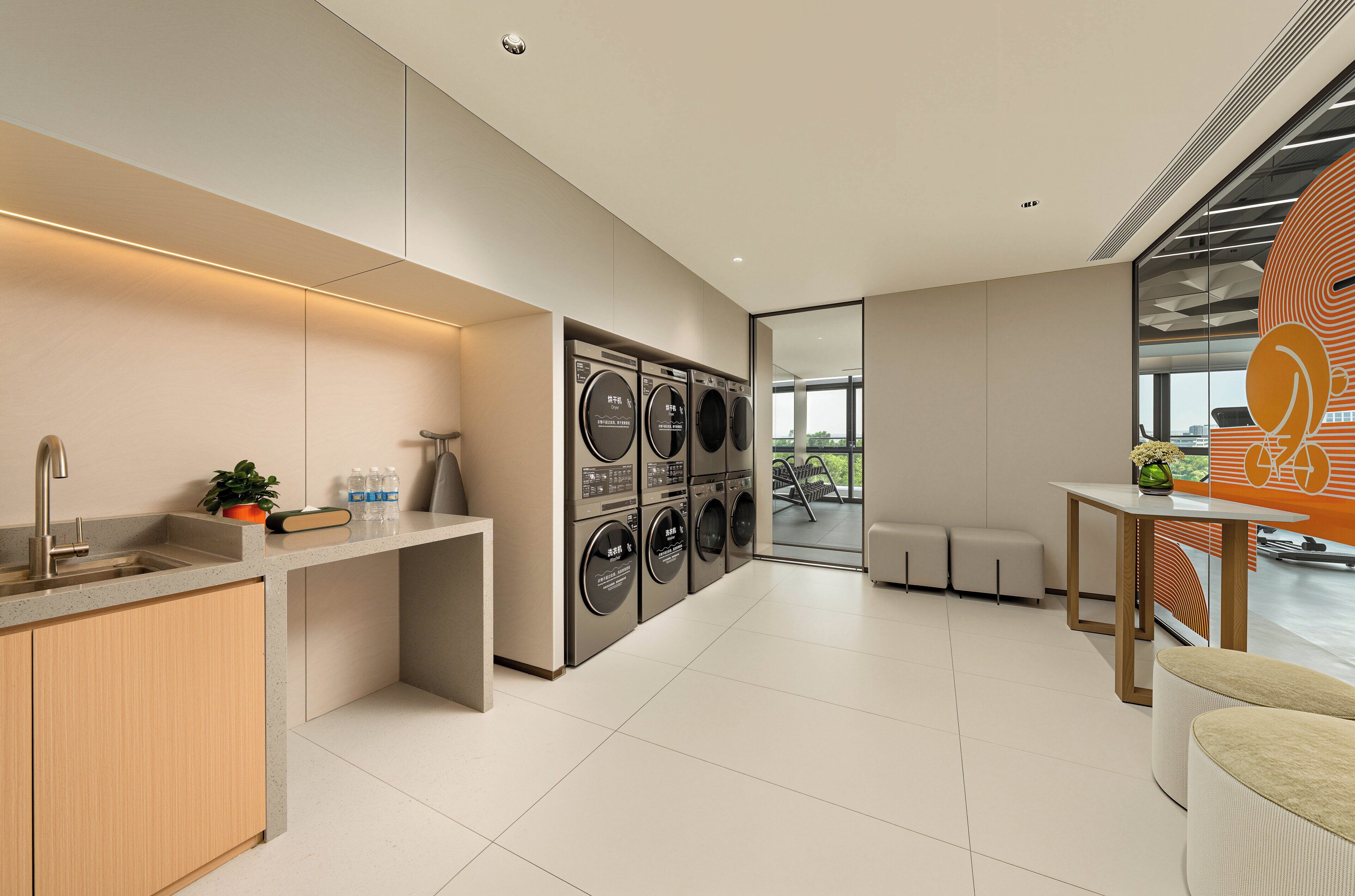 A modern laundry room with a washing machine and dryer, a sink, and a small table with a plant.