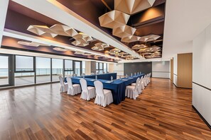 A conference room with a long table, white chairs, and a view of the sea through large windows.