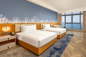 A hotel room with two beds, a desk, a lamp, and a view of the sea. - EVEN Hotel Yantai Golden Coast By IHG (Yantai)