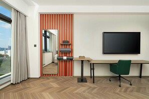 A hotel room with a desk, chair, and a large window.