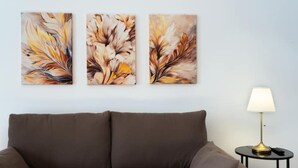 Un sofá marrón, una lámpara y tres cuadros abstractos en la pared.