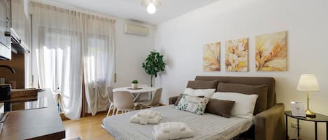 Une chambre d’hôtel comprenant un lit, une table de chevet, une lampe, un appareil de climatisation et un coin repas avec une table et des chaises.