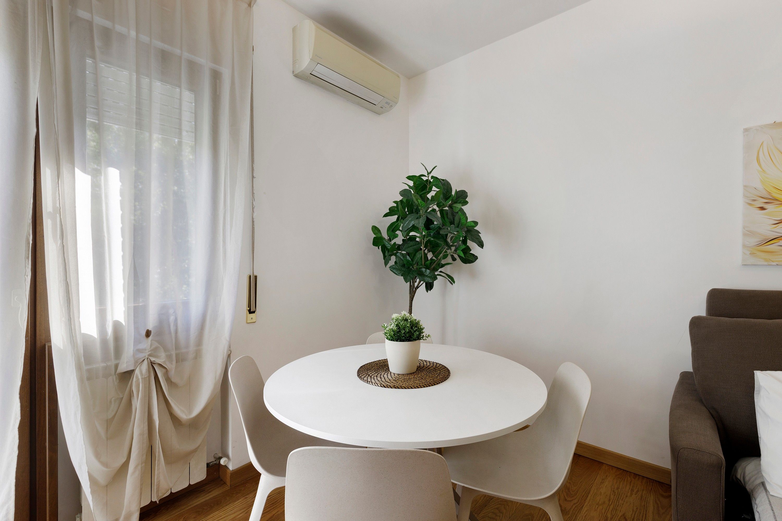 A dining area with a round table, chairs, a potted plant, and an air conditioning unit on the wall.