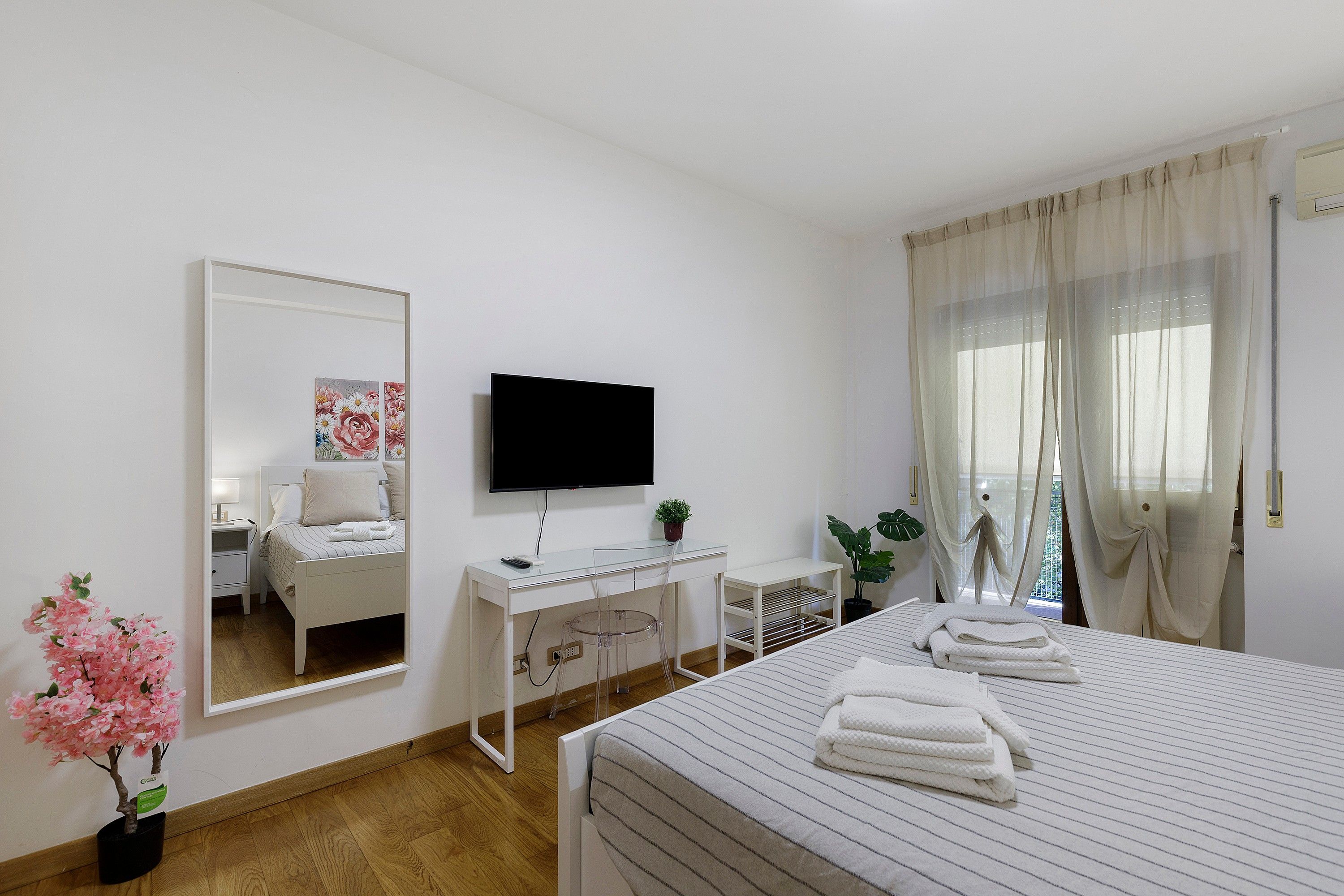 Ein Hotelzimmer mit Bett, Schreibtisch, Fernseher, Spiegel und einem Fenster mit Vorhängen.