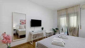 Ein Hotelzimmer mit Bett, Schreibtisch, Fernseher, Spiegel und einem Fenster mit Vorhängen.