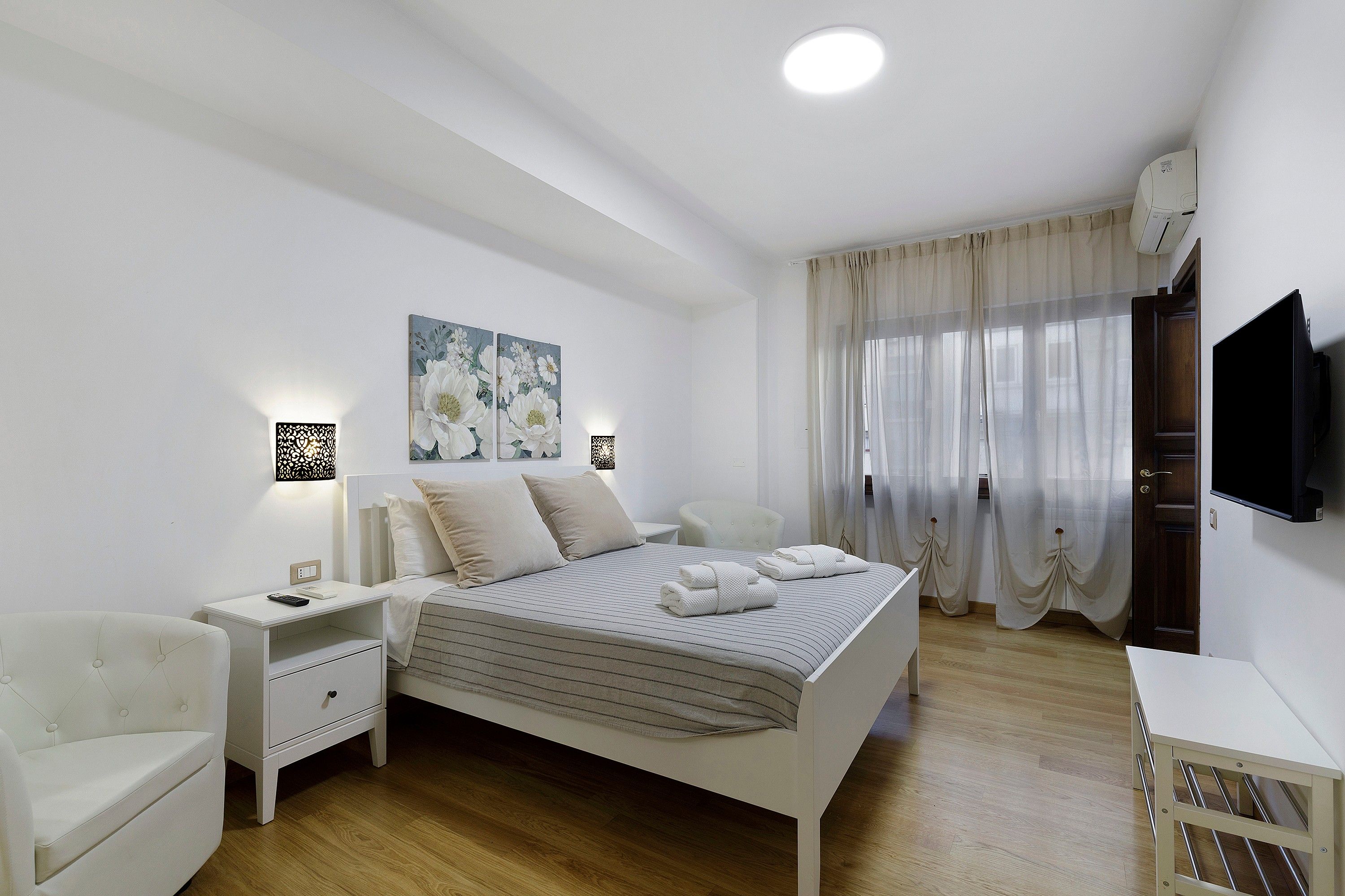 A bedroom with a bed, bedside tables, a chair, a TV, and a painting on the wall.